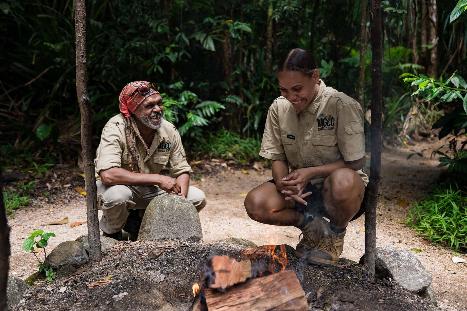Two Mossman Gorce guides laughing by a wood fire surrounded by leafy rainforest